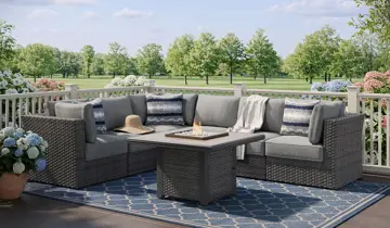 Grey wicker sectional, fire pit table, and blue rug on an outdoor deck