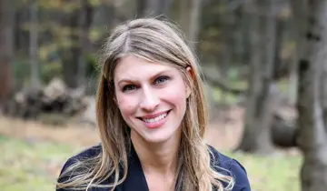 Blonde woman smiling outdoors with blurred trees in the background