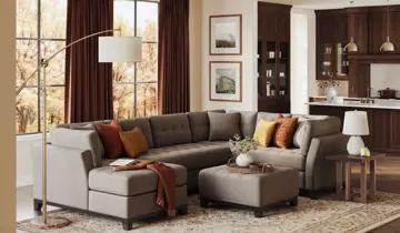Living room with gray L-shaped sectional sofa, ottoman, and dark wood kitchen