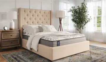 Bedroom with beige tufted bed, mattress, nightstand, lamps, and a plant