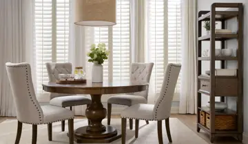 Dining room with round wooden table, four upholstered chairs, and tall display shelf