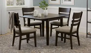 A cozy dining area features a dark wood square table and four matching chairs with light seats on a patterned rug