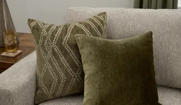 Two olive green pillows on a light-colored sofa with a partially visible side table