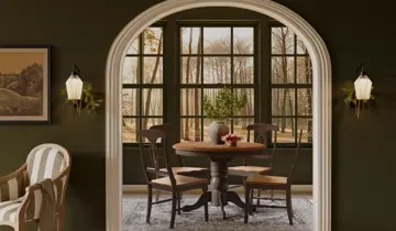 Arched doorway opens to dining room with round table, chairs, and forest view