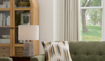 Living room with green sofa, patterned pillow, lamp, cabinet, and window view
