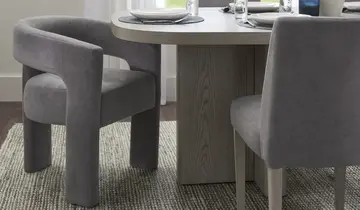 Gray velvet dining armchair and side chair with a light wood table on a textured rug