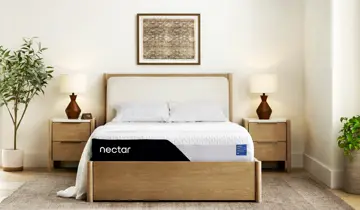 A light-toned bedroom with a bed, white mattress, two nightstands, and plants