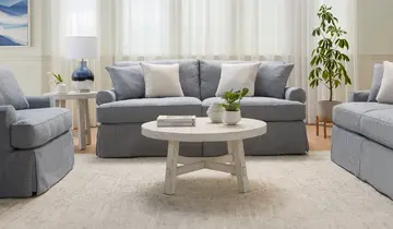 Bright living room with light blue slipcovered furniture, white tables, and a large neutral area rug