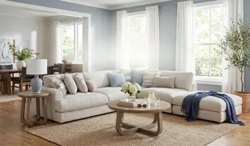 Light blue living room with large beige sectional, round coffee table, and potted tree