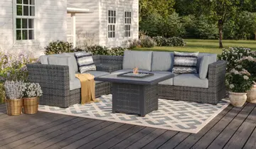 Wicker patio sectional with gray cushions and fire pit table on a wooden deck