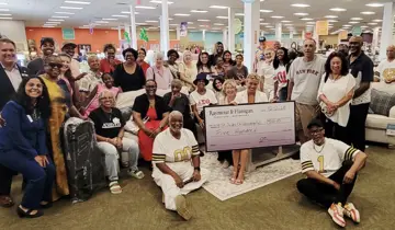 Large diverse group poses with an oversized check in a furniture store