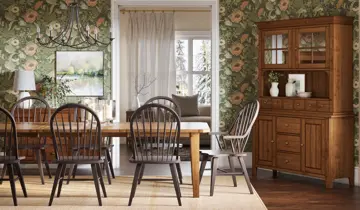 Dining room with wooden table, chairs, hutch, floral wallpaper, and winter scene