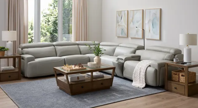 Airy living room with light gray leather sectional, wooden tables, blue rug, and natural light from large windows