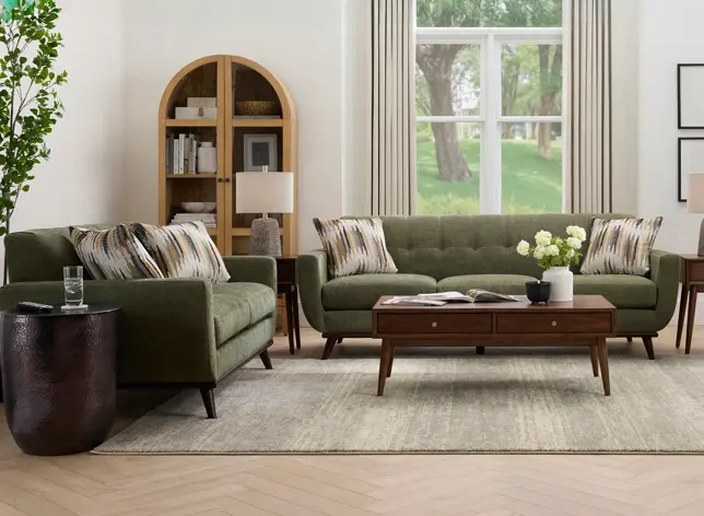 Bright modern living room with olive green sofas, wood coffee table, arched bookshelf, and window view