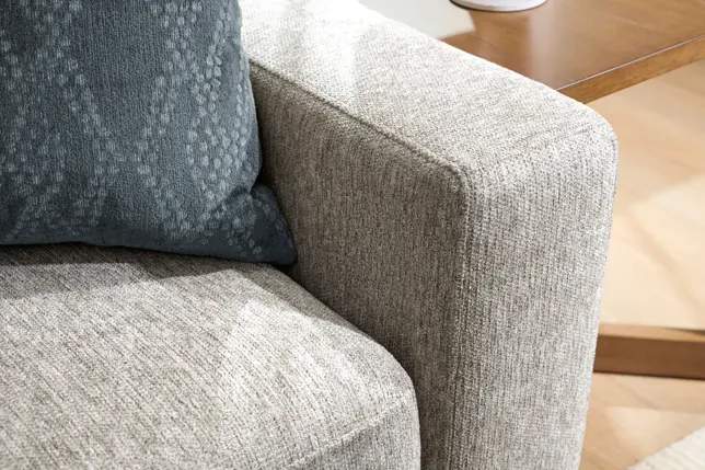 Light gray textured sofa with a dark teal patterned pillow and a partial wooden side table