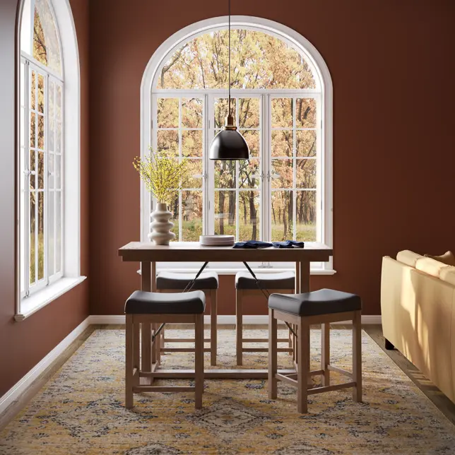 A cozy room with warm brown walls, a counter-height dining set, and arched windows looking out to autumn trees