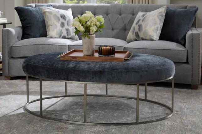 Cozy living room with a gray tufted sofa, a dark blue velvet oval ottoman, and elegant decorative accents