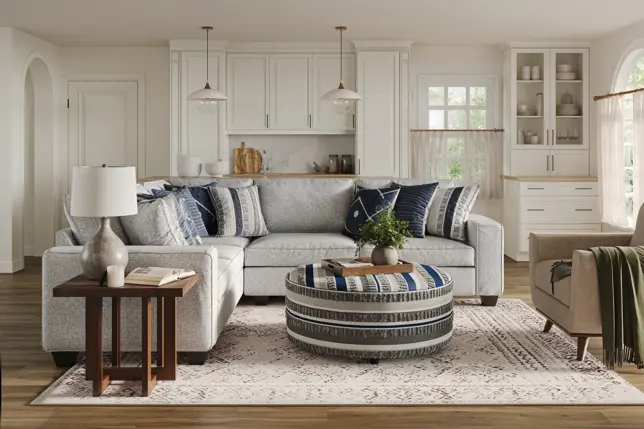 Cozy living room with a light gray sectional, blue throw pillows, round striped ottoman, and wooden side table