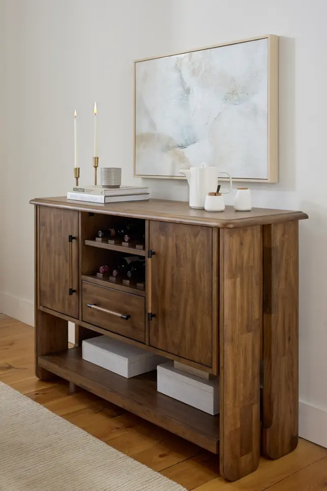 Warm-toned wooden sideboard with wine rack, styled with candles, books, and abstract art in a minimalist room