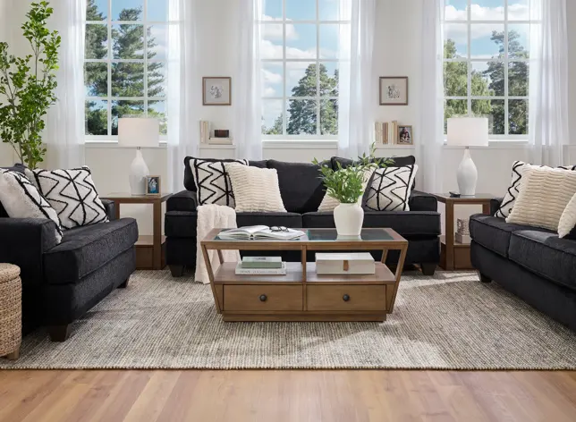 Bright living room with two charcoal sofas, patterned pillows, a wood coffee table, and large windows