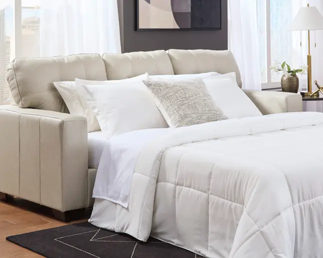 A modern light beige sofa sleeper extended into a bed with white bedding, pillows, and a textured throw pillow
