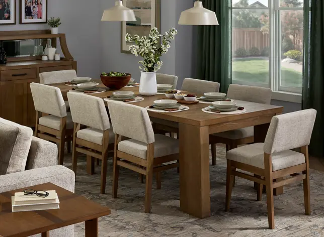 Warm dining room with a long wooden table, light upholstered chairs, buffet, and adjacent living area