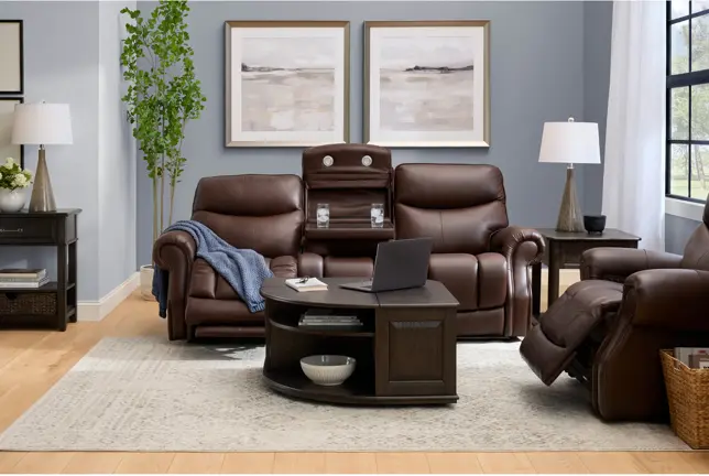 Cozy living room with brown leather reclining sofas, an armchair, dark wood tables, and a light rug