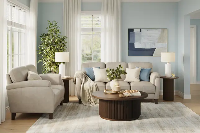 Light blue living room with beige sofa, matching armchair, dark wood tables, and a light patterned rug