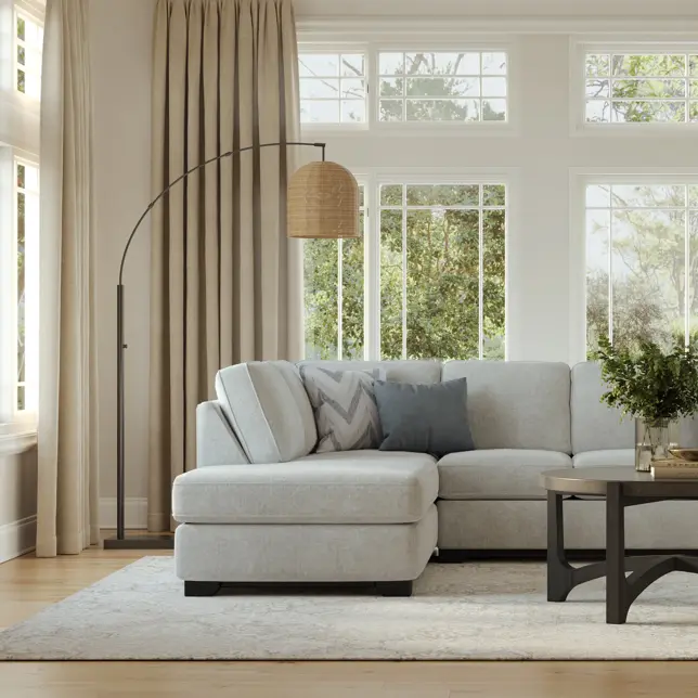 Bright living room with light gray sectional, arched lamp, coffee table, and large windows with green views