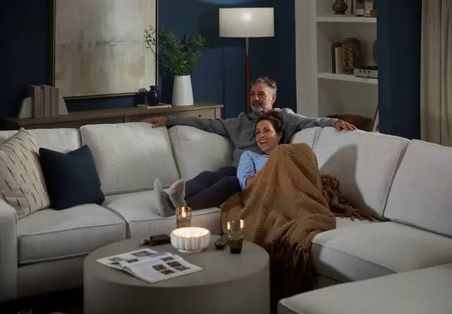 Cozy living room with a couple relaxing on a light sectional sofa, coffee table, and dark blue accent wall