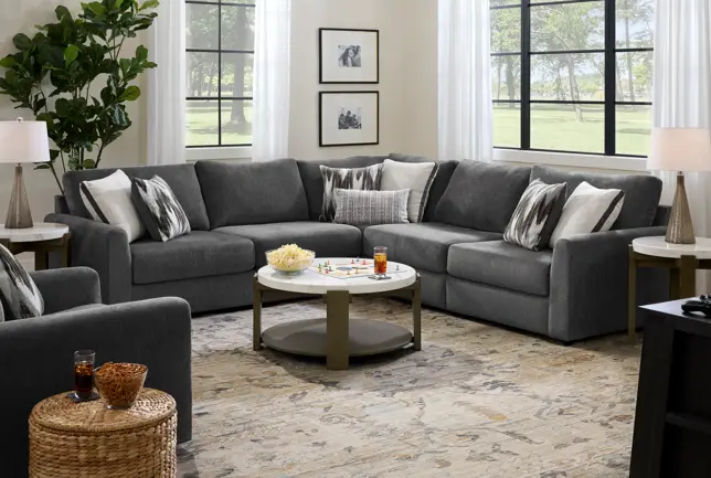 Well-lit living room with a large dark gray L-shaped couch, an armchair, coffee table, and patterned rug