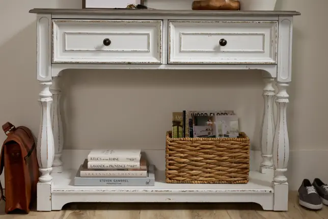 Distressed white and grey console table featuring drawers, a lower shelf, a basket, stacked books, and personal items
