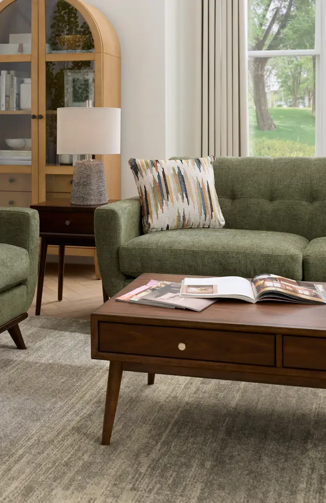 Living room with green sofa, wooden tables, display cabinet, rug, and window view