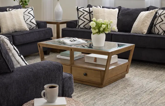 Cozy living room featuring dark gray sofas, a wood and glass coffee table, and patterned pillows on a light rug