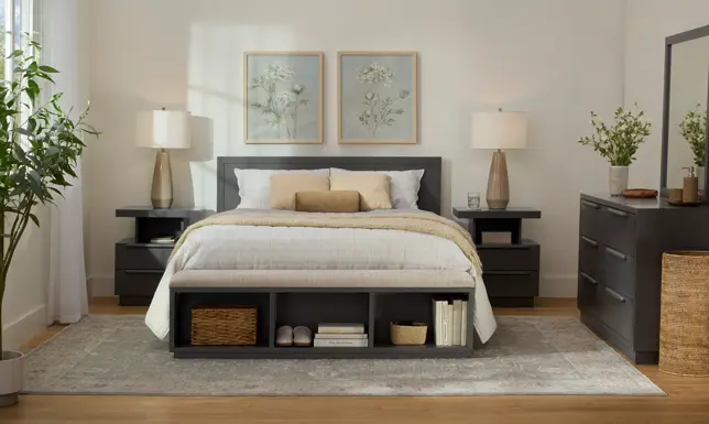 Bright bedroom with gray bed, nightstands, storage bench, dresser, botanical art, and light gray rug