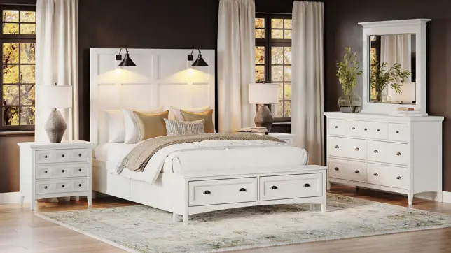 Bright bedroom featuring a white storage bed, nightstands, and dresser, set against a dark wall with large sunlit windows