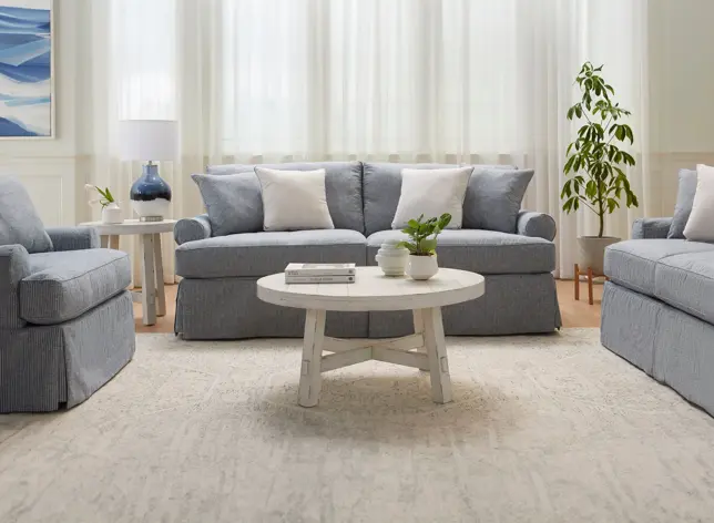 Light-filled living room with blue and white striped slipcovered sofas, armchair, white tables, and green plant
