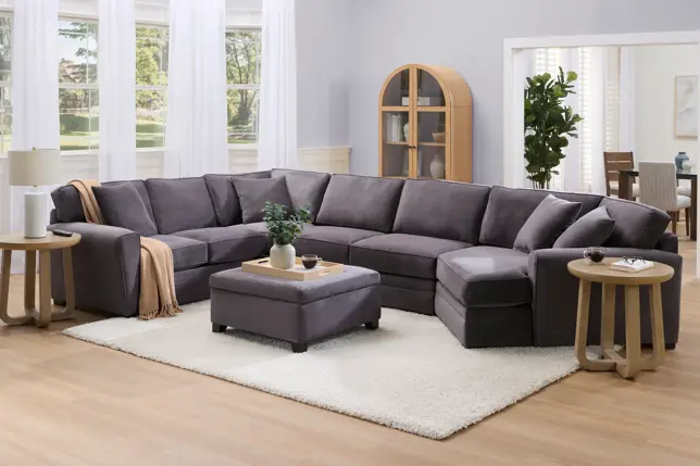 Modern living room with a spacious gray U-shaped sectional sofa, ottoman, white rug, and light wooden accents