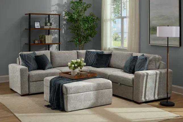 Cozy gray living room with an L-shaped sectional sofa, matching ottoman, bookshelf, and large window