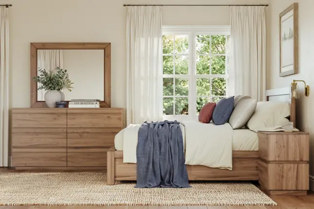 Bright bedroom with light wood furniture, white bedding, blue throw, mirror, and a sunny window view