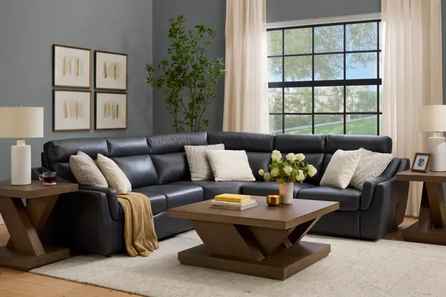 Modern living room featuring a dark gray leather L-shaped sectional, wood tables, neutral decor, and natural light