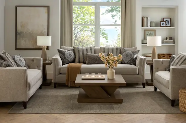 Neutral living room with gray sofa, two armchairs, wooden coffee table, and built-in shelves, bright with natural window light