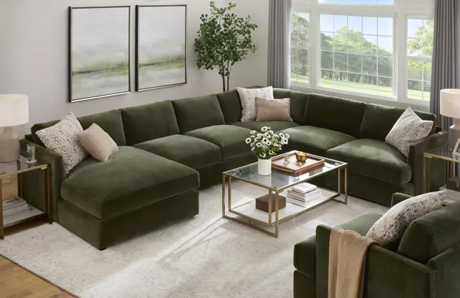 Modern living room features a large olive green U-sectional, matching armchair, bright windows, and a glass coffee table