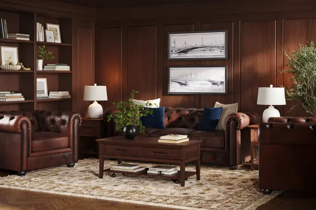 Warm, wood-paneled study featuring brown leather tufted sofa and armchairs, dark wood tables, and a light patterned rug