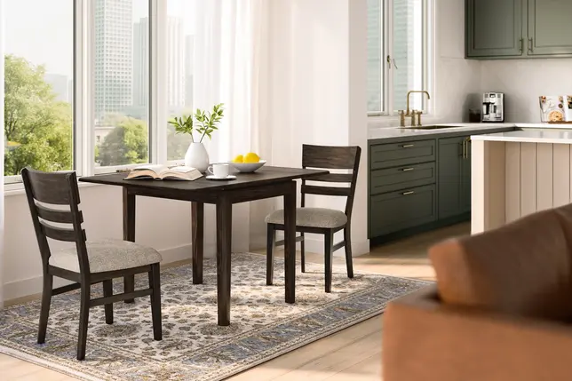 Bright dining area with dark wood table and chairs, patterned rug, kitchen, and large windows