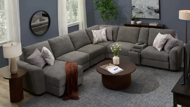Modern living room with a large gray modular sectional, dark wood tables, textured rug, and accent pillows