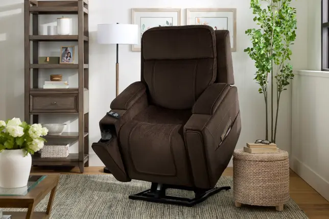 Cozy living room with a brown recliner, wooden bookshelf, woven ottoman, and floor lamp on a rug