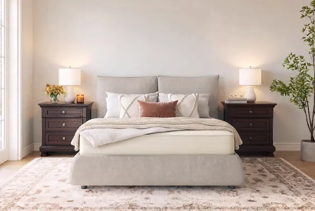 A neutral-toned bedroom with a light grey upholstered bed, dark wood nightstands, lit lamps, and a patterned area rug