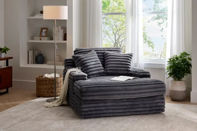 Cozy living room with a large, ribbed gray lounge chair, floor lamp, and bright window with sheer curtains